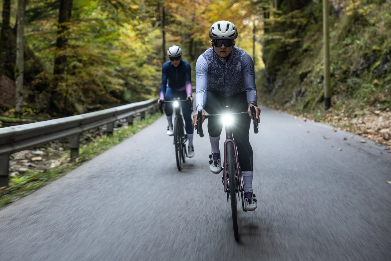 Zwei Radfahrerinnen mit Rücklichtern auf kurviger Straße
